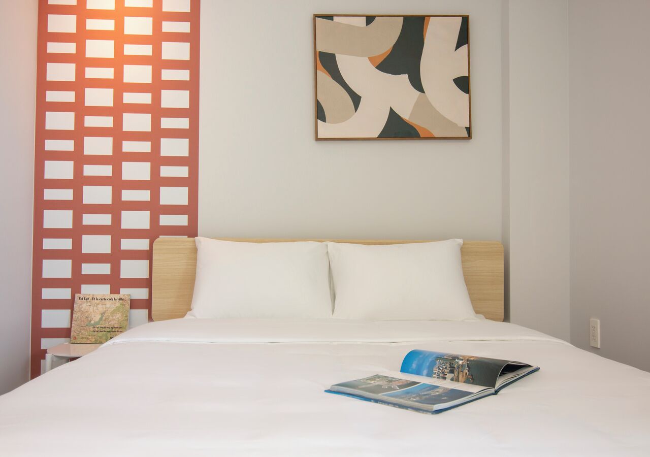 A hotel room with a bed, a map on the nightstand, and a wall with abstract art.