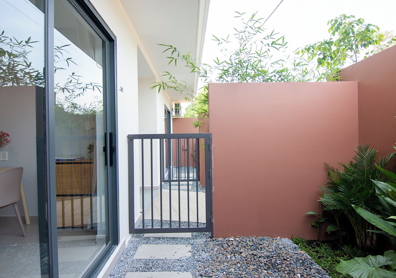 Un espacio exterior moderno con un ventanal de vidrio que da a un patio, una reja metálica y un pequeño jardín de piedras y plantas.