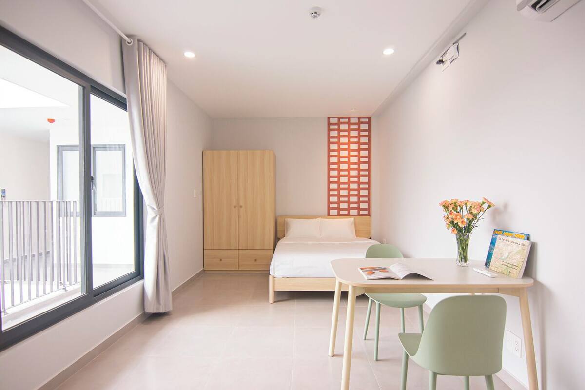 Ein modernes Schlafzimmer mit einem Bett, einem Schreibtisch mit Stühlen, einem Fenster mit Vorhängen und einem Holzschrank.