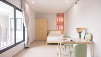 A modern bedroom with a bed, a desk with chairs, a window with curtains, and a wooden wardrobe.