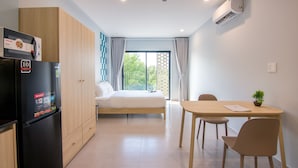 A modern hotel room with a bed, a dining table with chairs, a refrigerator, and an air conditioning unit. - ORA Serviced Apartments - Binh Duong New City (Ho Chi Minh City)