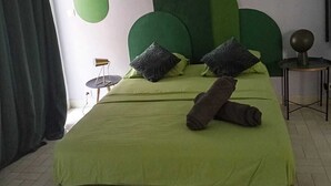 Un dormitori amb un llit, roba de llit verda, un capçal de llit verd i singular, una petita taula de nit i un aparell d'aire condicionat.