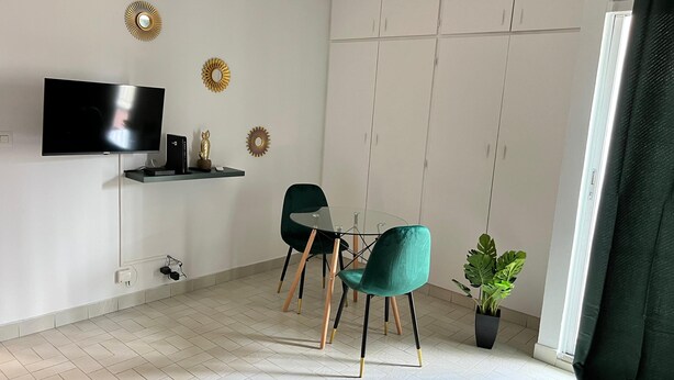 Un saló modern amb televisió de pantalla plana, dues cadires color turquesa, una taula de vidre i miralls decoratius a la paret.