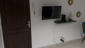 Habitació amb una porta de fusta fosca, un televisor de pantalla plana fixat a la paret, una petita estant amb un altaveu, decoració mural i una presa elèctrica.