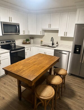 Una cocina moderna con armarios blancos, electrodomésticos de acero inoxidable, una mesa de comedor de madera y taburetes de mimbre.