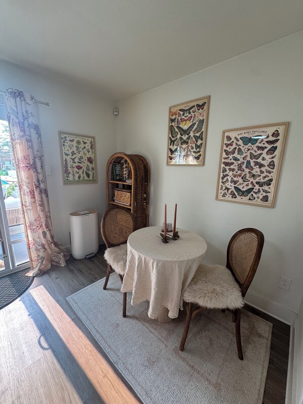 Un comedor con una mesa redonda, dos sillas, una estantería y un cuadro de mariposas en la pared.