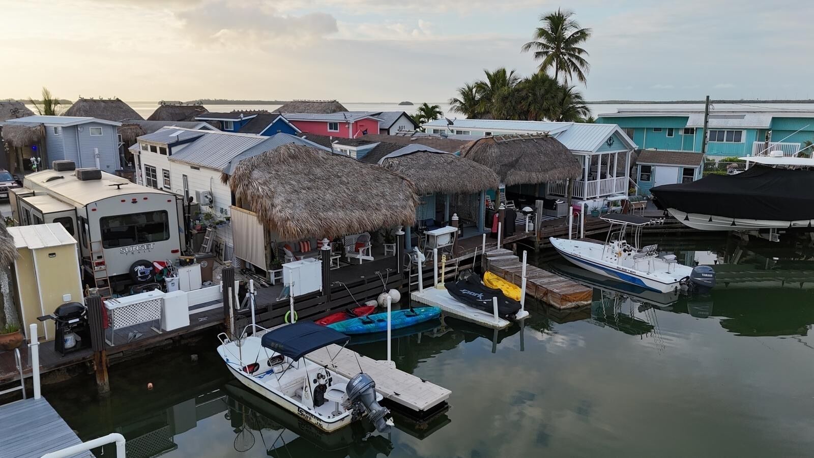 A marina with boats docked, thatched-roof structures, and a trailer in the foreground.