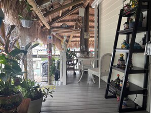 A covered outdoor area with a wooden floor, white wicker furniture, and a variety of potted plants. - Nice Water Front Tiny home w AC, WiFi include boat ramp & 20ft dock in KeyLargo (Key Largo)