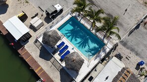 An aerial view of a pool area with a clear blue pool, lounge chairs, and palm trees. - Nice Water Front Tiny home w AC, WiFi include boat ramp & 20ft dock in KeyLargo (Key Largo)