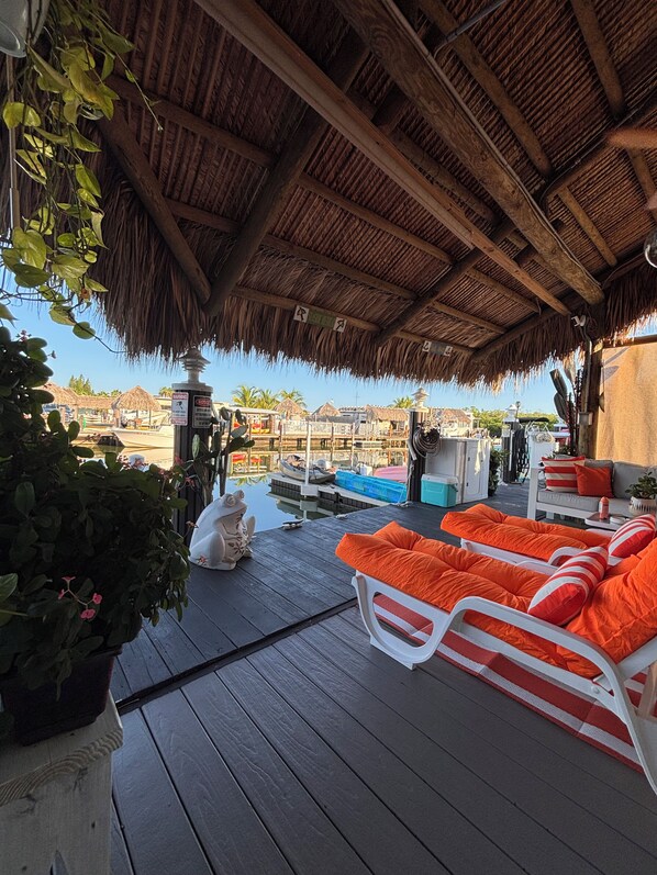 A covered outdoor area with a wooden deck, lounge chairs, and a view of a water body.
