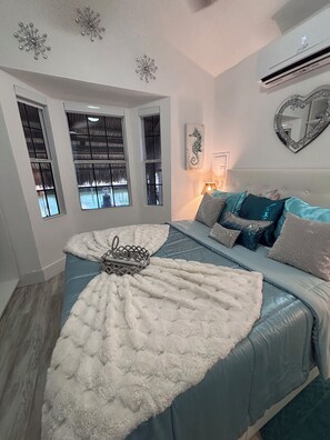 A bedroom with a bed, a window, a wall-mounted mirror, and a decorative seahorse painting.
