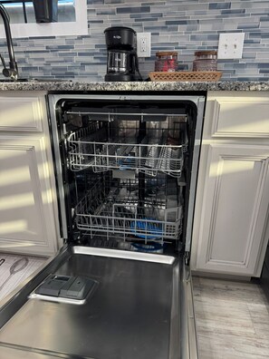 An open dishwasher with multiple racks and a stainless steel interior.