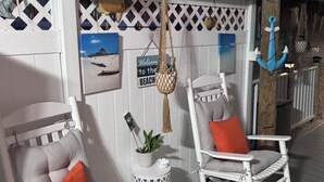 Two white rocking chairs with orange cushions, a small white side table with a plant, and a sign that reads "Welcome to the Beach". - Nice Water Front Tiny home w AC, WiFi include boat ramp & 20ft dock in KeyLargo (Key Largo)