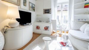 A modern, white-themed living room with a flat-screen TV, a white sofa, a dining table, and a kitchen area with a microwave. - Sant' Andrea Fashion Suite by Interhome (Milan)