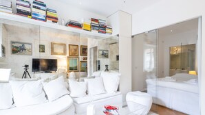 A modern living room with a white sofa, a glass coffee table, and a mirrored wall reflecting the room. - Sant' Andrea Fashion Suite by Interhome (Milan)
