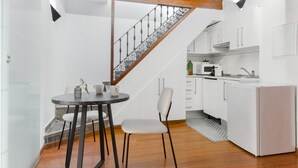 A modern kitchen with white cabinets, a microwave, and a sink. There is a dining area with a round table and two chairs. A staircase with a metal railing leads to an upper level. - Apartment with a spectacular terrace in the center (Málaga)