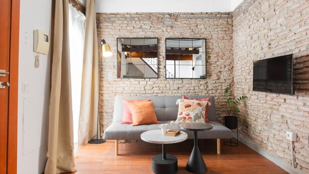 A cozy living room with a brick wall, a grey sofa, a round coffee table, and a flat-screen TV mounted on the wall. - Apartment with a spectacular terrace in the center (Málaga)