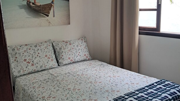 A bed with floral bedding, a patterned throw, and a painting of a boat on water.