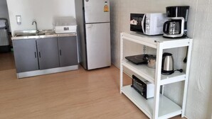 Een compact keukenhoekje met een koelkast, magnetron, koffiezetapparaat en een plank met waterkoker en pannen.