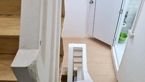 Een houten trap met witte leuningen, die leidt naar een witte deur en een klein houten krukje.