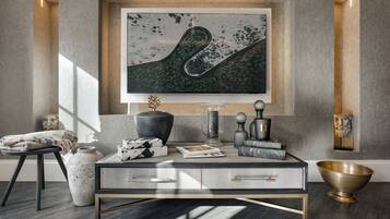 A modern living room with a glass coffee table, a framed abstract painting, and a decorative bowl.