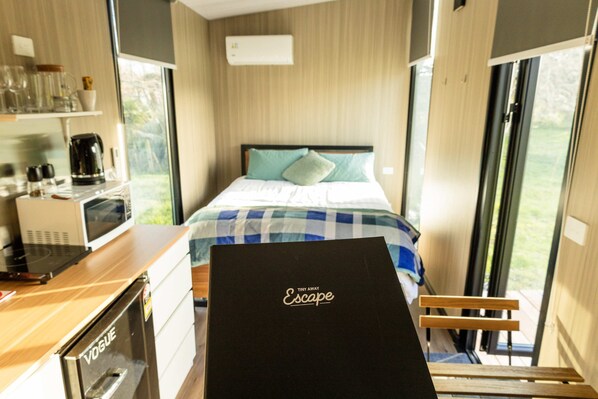 A compact room with a bed, a kitchenette, and a view through a door.