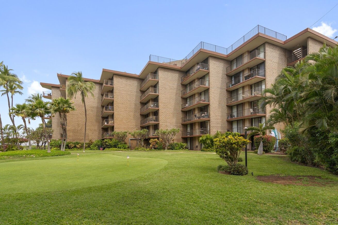 A multi-story hotel with a brick facade, multiple balconies, and a well-maintained lawn.