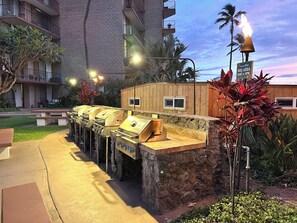 An outdoor barbecue area with multiple grills, a wooden structure, and a sign indicating BBQ hours.