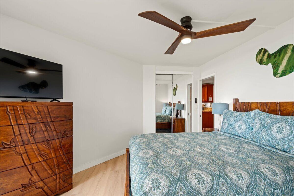 A bedroom with a bed, a wooden dresser, a ceiling fan, a television, and a green wall decoration.