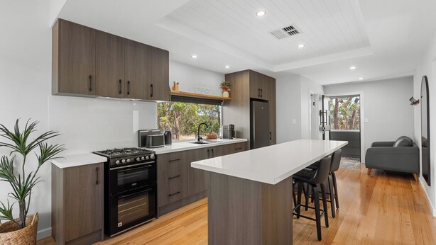 Een moderne keuken met donkerhouten kasten, een centraal eiland met barkrukken, een ingebouwde oven en een groot raam met uitzicht op de omgeving.