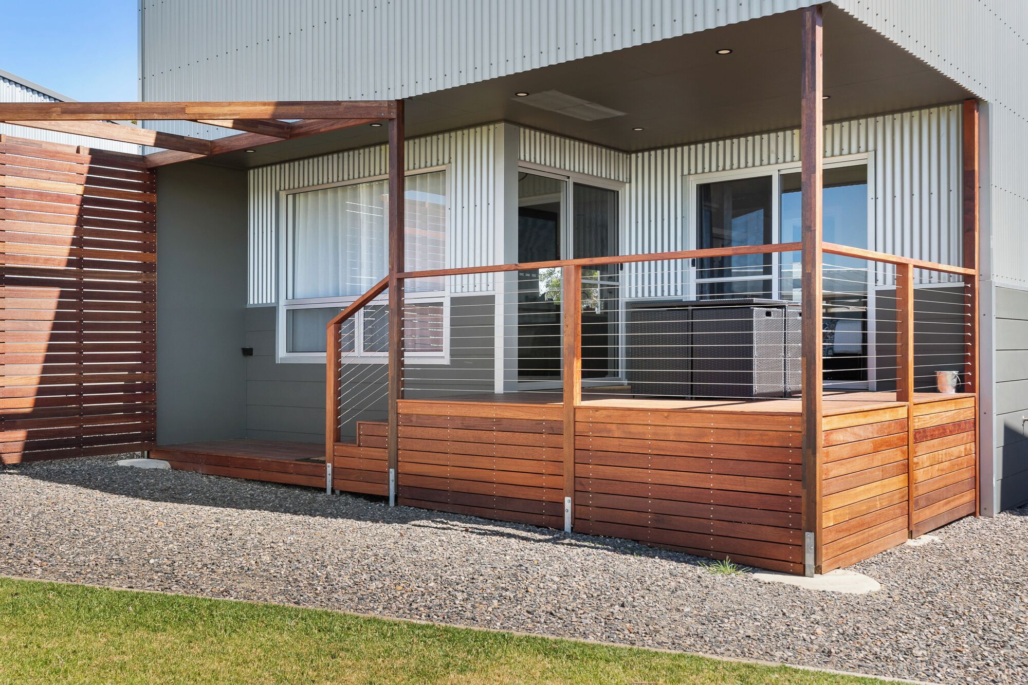 A modern house with a wooden deck, large windows, and a metal railing.