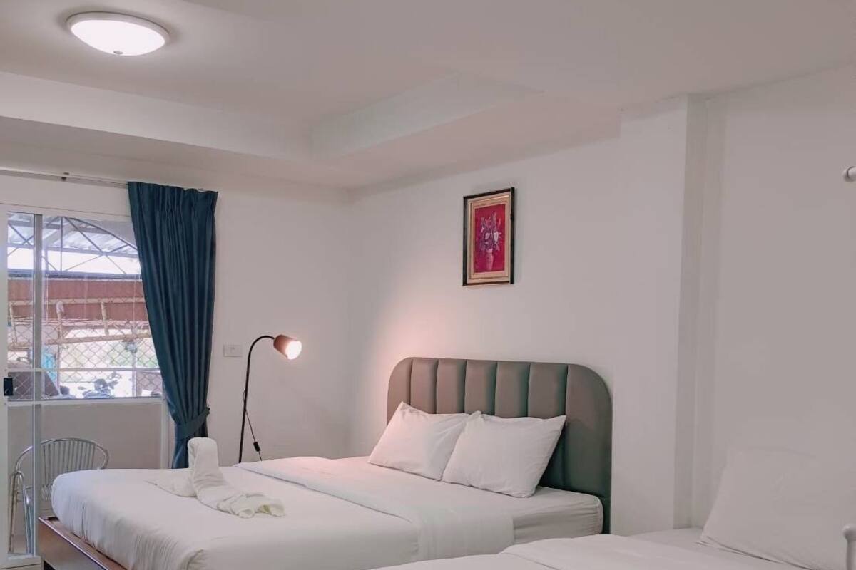 A hotel room with two beds, a large window with blue curtains, a ceiling light, and a framed picture on the wall.