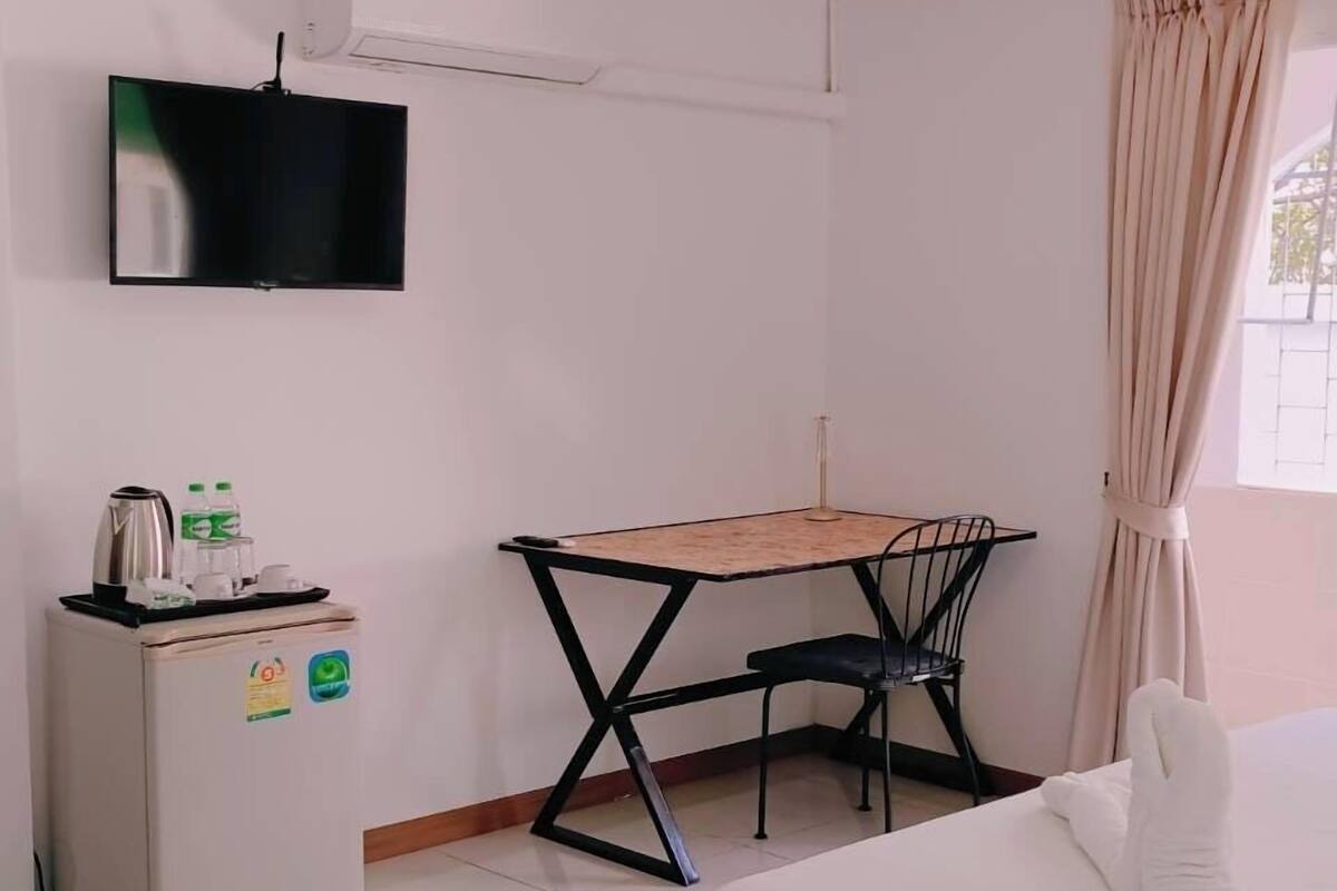 A hotel room with a bed, a desk, a TV, an air conditioner, and a window with curtains.