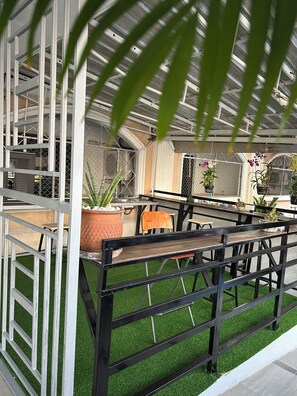 A covered outdoor seating area with artificial grass, metal railings, and potted plants. - Convenient Resort  (Bangkok)