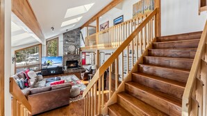 Un salón amplio con escalera de madera, chimenea de piedra y televisor grande.
