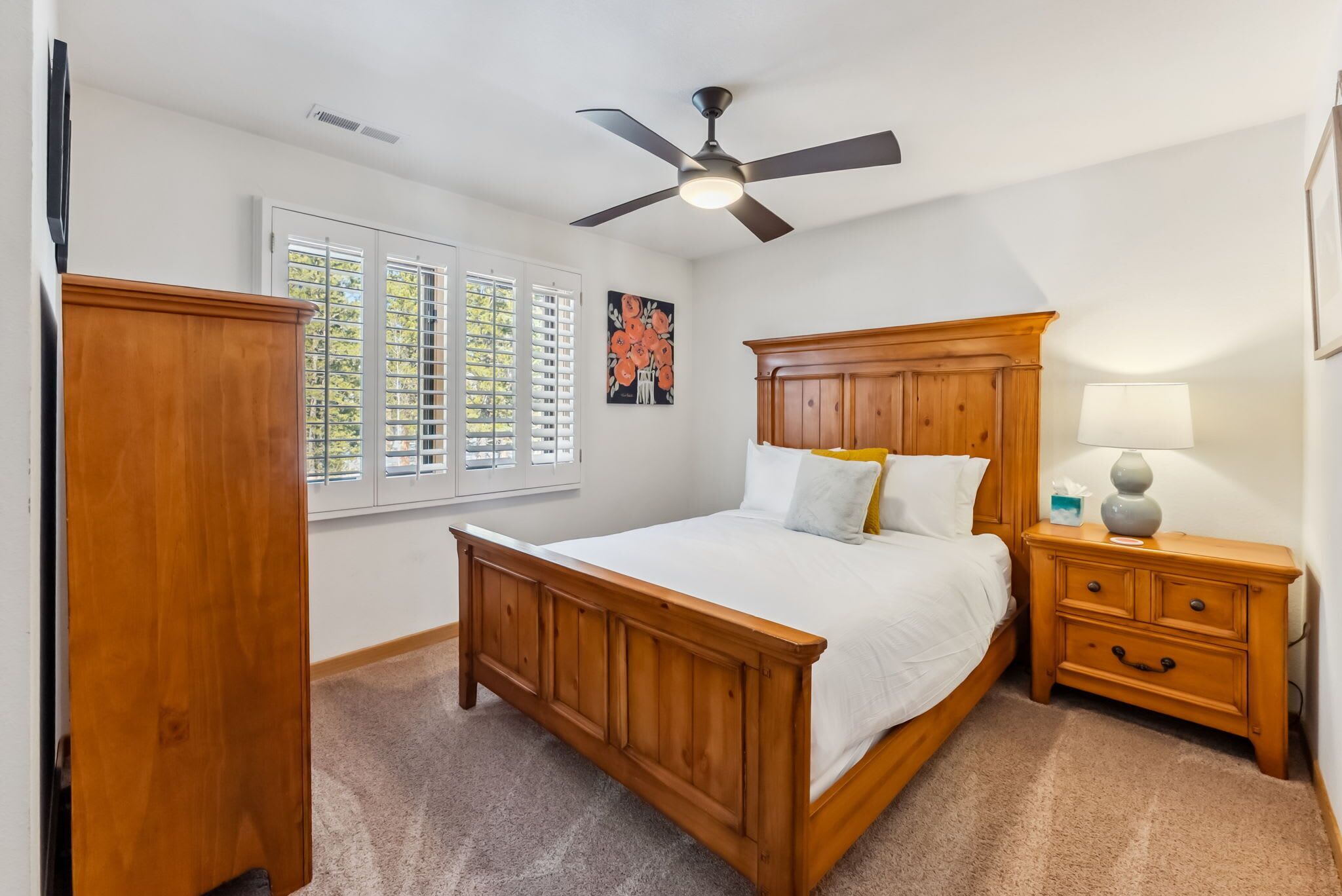 A bedroom with a wooden bed, a nightstand, a ceiling fan, and a window with blinds.