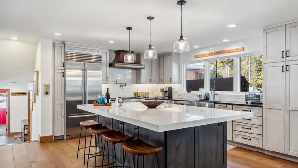 Una cocina moderna con una isla grande, electrodomésticos de acero inoxidable e iluminación colgante.