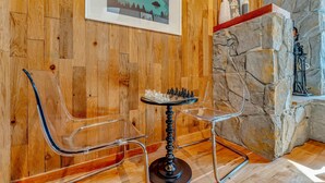 A wooden-paneled room with a chess table and chairs, stone wall, and framed artwork.