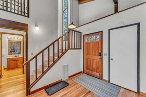Eine Treppe mit Holzwerteln führt zu einer zweiten Etage, eine Holztür mit Fenster und eine Leuchte darüber.