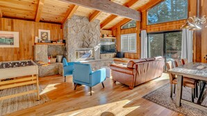 A spacious wooden cabin interior with a stone fireplace, a dining area, and a cozy seating area.