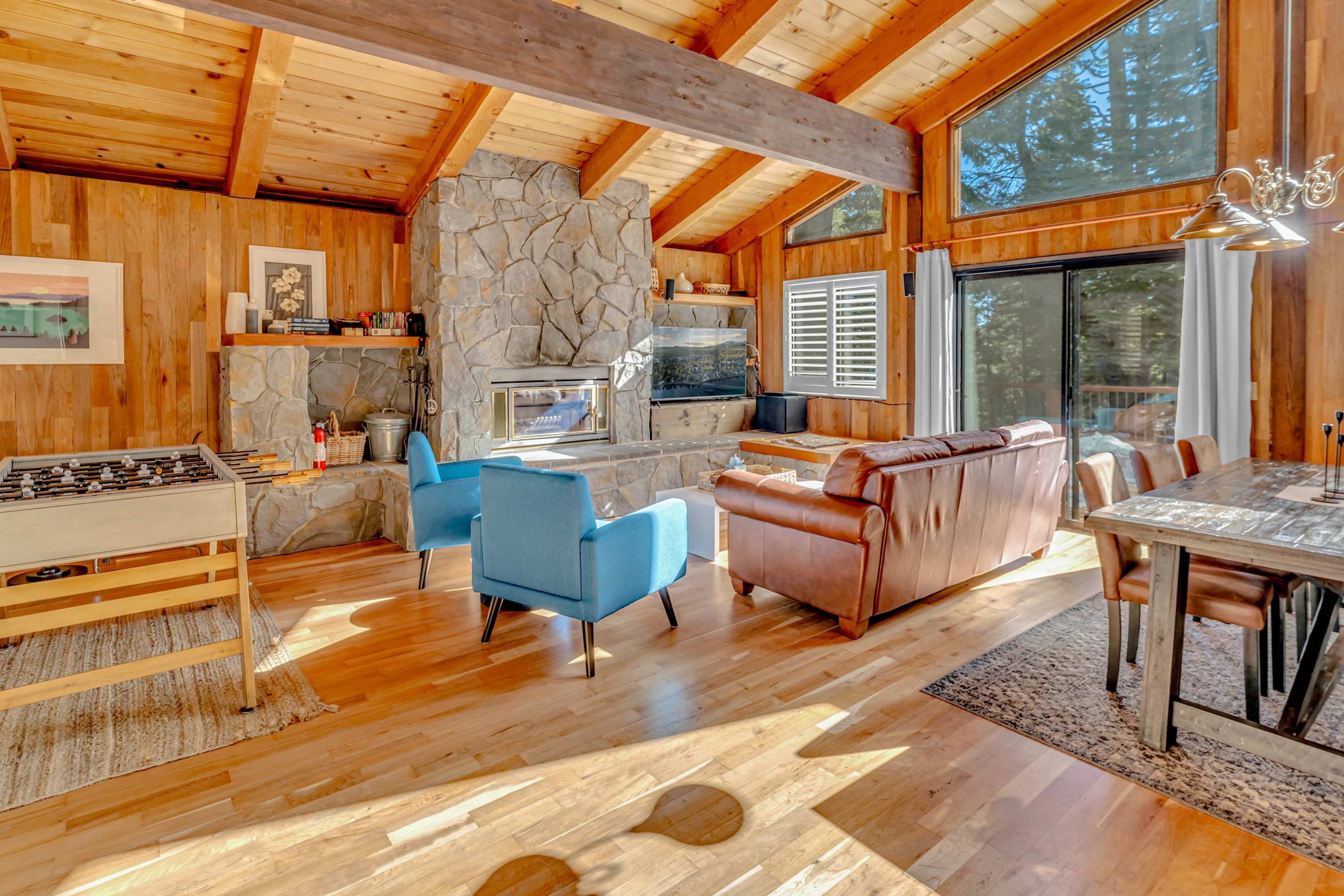 A spacious wooden cabin interior with a stone fireplace, a dining area, and a cozy seating area.