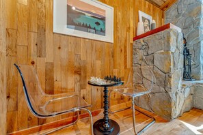 A wooden-paneled room with a chess table and chairs, stone wall, and framed artwork.