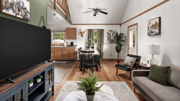 A spacious living room with a ceiling fan, a TV, a dining area with a table and chairs, a sofa, and a kitchen in the background. - Mountain retreat chalet w/ hot tub & deck (Rio)