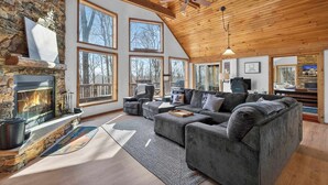 A spacious living room with a stone fireplace, large windows, and a cozy seating area. - Cabin w/hot tub, fire pit & deck (Hedgesville)