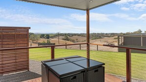 Un balcone con vista su un paesaggio rurale, una recinzione in legno e un tavolino in vimini.