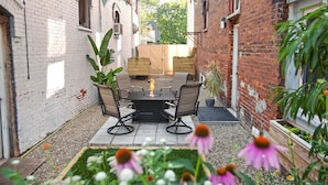 A patio with a fire pit table and chairs, surrounded by brick walls and potted plants.