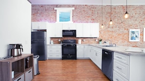 A modern kitchen with white cabinets, a black stove, and a brick wall.