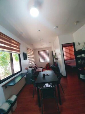 A dining area with a table and chairs, a bench, and a window with blinds. - Casa Rafael Coron (Coron)
