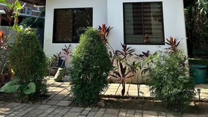A small, single-story house with a white exterior and a brown roof, surrounded by lush greenery and trees. - Casa Rafael Coron (Coron)