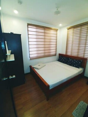 A bedroom with a bed, two windows with blinds, a wardrobe, and a small rug. - Casa Rafael Coron (Coron)